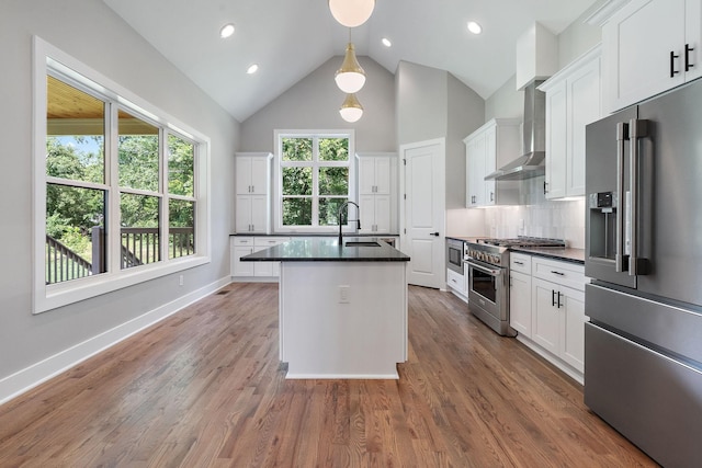 kitchen with high end appliances, wall chimney range hood, white cabinets, backsplash, and an island with sink