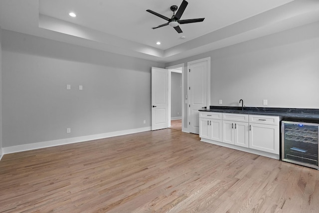 bar with white cabinets, light hardwood / wood-style flooring, a tray ceiling, and beverage cooler