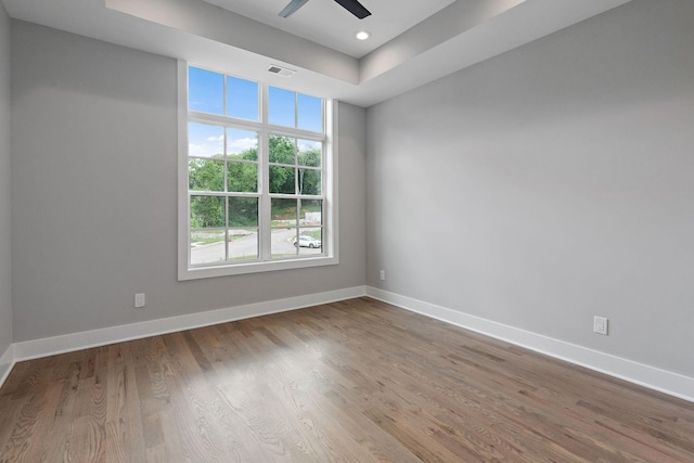 unfurnished room with ceiling fan, light wood-type flooring, and a tray ceiling