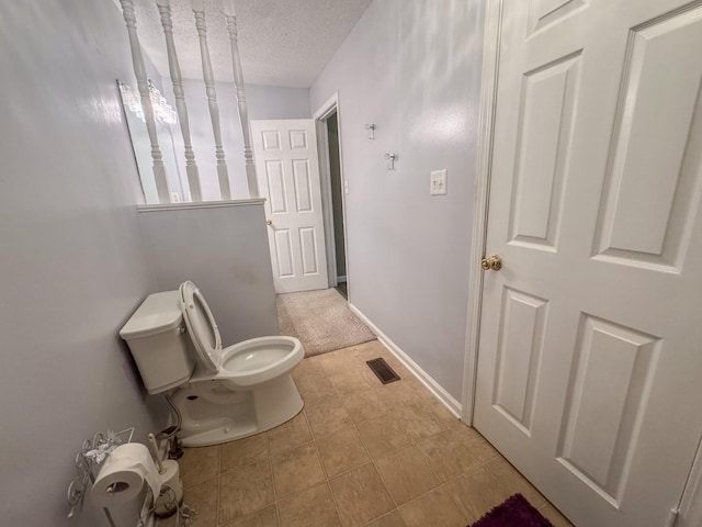 bathroom featuring tile patterned floors, visible vents, toilet, a textured ceiling, and baseboards