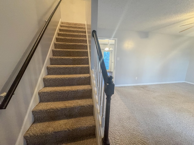 stairway featuring baseboards, carpet floors, and a textured ceiling