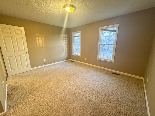 empty room with visible vents, a textured ceiling, baseboards, and carpet floors