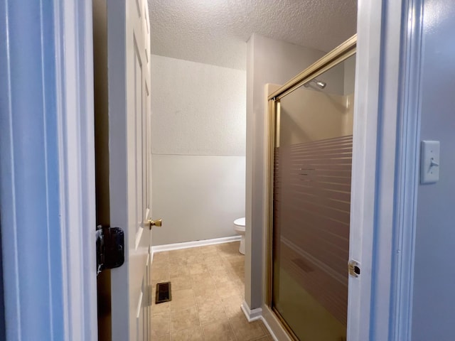 bathroom featuring a shower stall, a textured ceiling, toilet, and baseboards