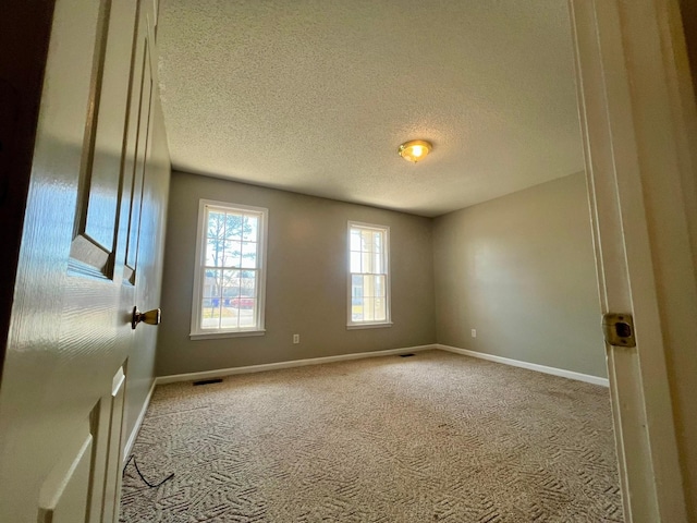 empty room with visible vents, baseboards, a textured ceiling, and carpet flooring