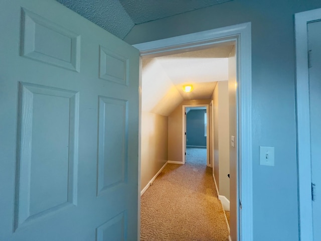 corridor featuring lofted ceiling, light colored carpet, baseboards, and a textured ceiling