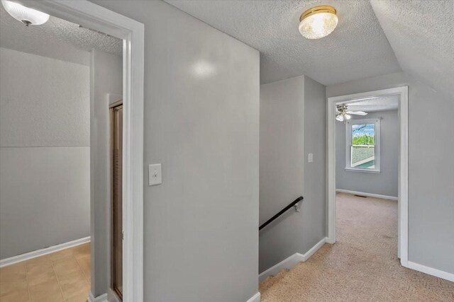 hallway with an upstairs landing, a textured ceiling, baseboards, and lofted ceiling