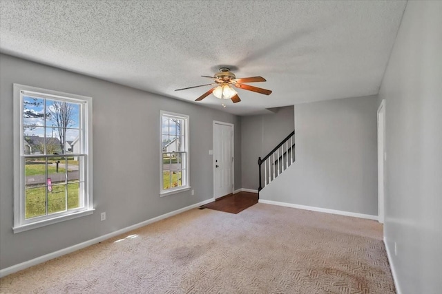 carpeted foyer entrance with a textured ceiling, ceiling fan, baseboards, and stairs