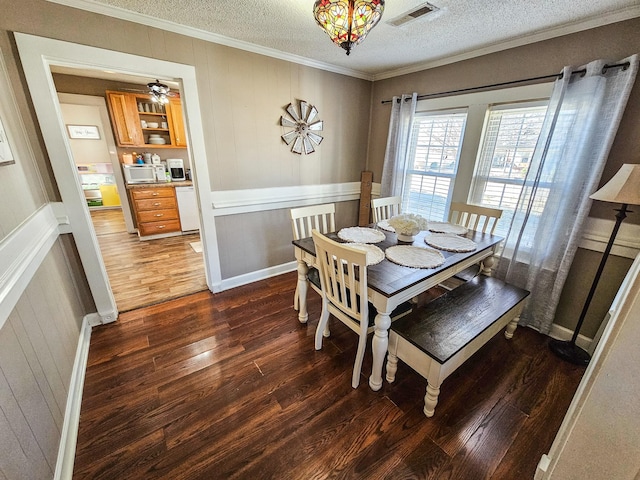 dining area with ornamental molding, a textured ceiling, dark hardwood / wood-style flooring, and wooden walls