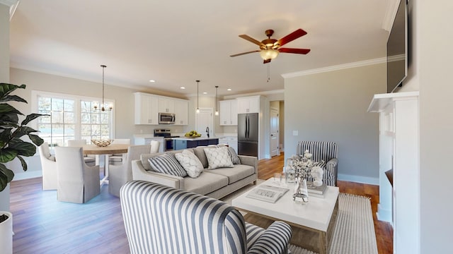 living room with light hardwood / wood-style flooring, ceiling fan with notable chandelier, crown molding, and sink