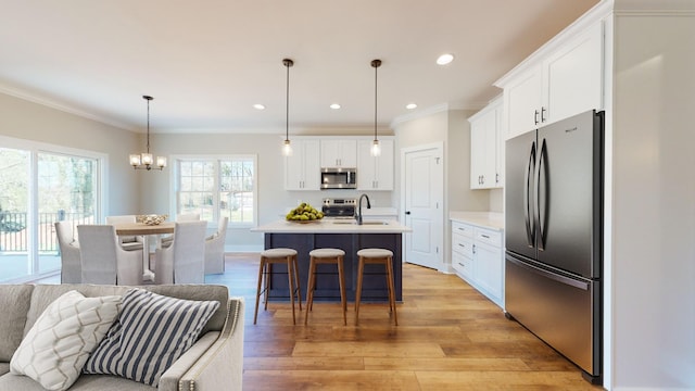 kitchen featuring crown molding, appliances with stainless steel finishes, white cabinetry, decorative light fixtures, and an island with sink