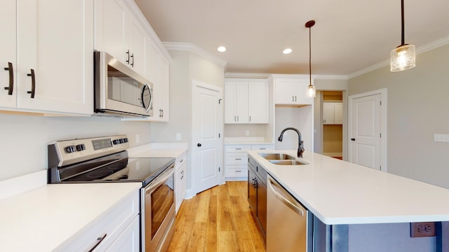 kitchen with crown molding, appliances with stainless steel finishes, white cabinetry, hanging light fixtures, and an island with sink