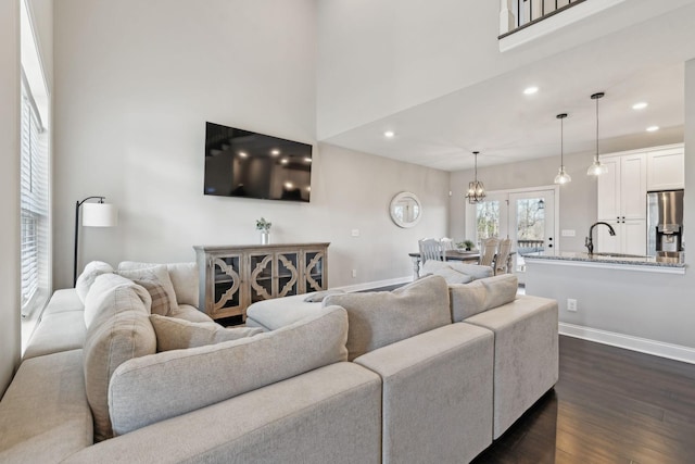 living room featuring sink, a towering ceiling, dark wood-type flooring, and a chandelier