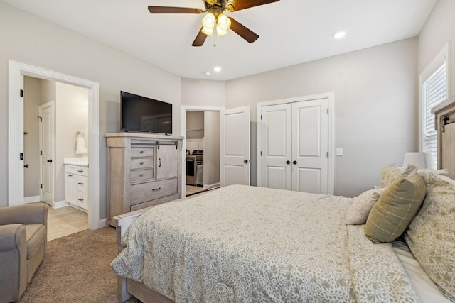 bedroom with ceiling fan, ensuite bath, light colored carpet, and a closet