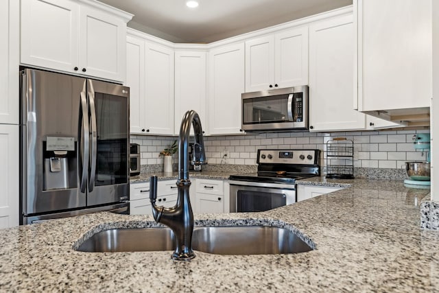 kitchen featuring stainless steel appliances, white cabinetry, and light stone countertops