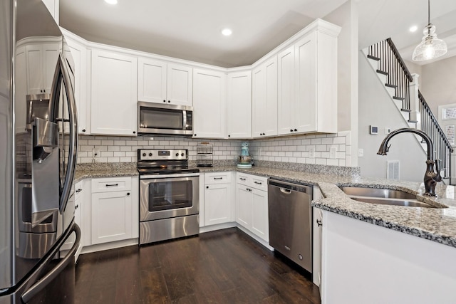 kitchen with appliances with stainless steel finishes, decorative light fixtures, sink, white cabinets, and light stone counters