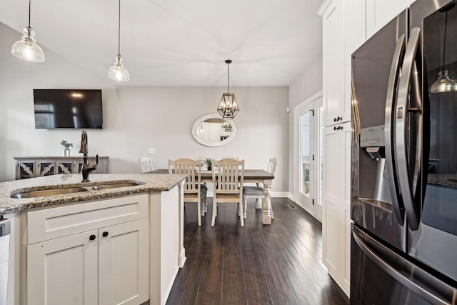 kitchen featuring sink, hanging light fixtures, stainless steel refrigerator with ice dispenser, light stone countertops, and white cabinets