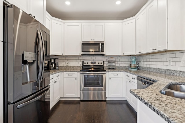 kitchen featuring tasteful backsplash, white cabinetry, stainless steel appliances, light stone countertops, and dark wood-type flooring