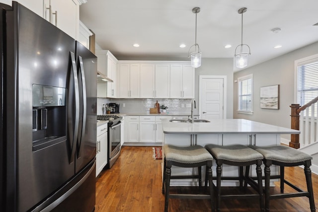 kitchen featuring white cabinets, stainless steel range oven, refrigerator with ice dispenser, sink, and a kitchen island with sink