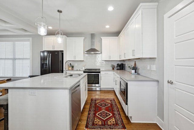 kitchen featuring white cabinets, appliances with stainless steel finishes, wall chimney exhaust hood, decorative light fixtures, and an island with sink