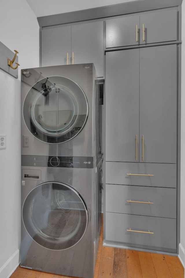 clothes washing area featuring cabinets and stacked washing maching and dryer