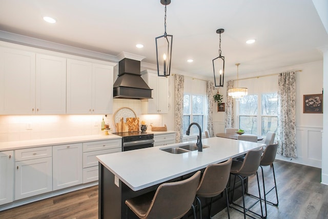 kitchen with premium range hood, pendant lighting, black electric range, and an island with sink