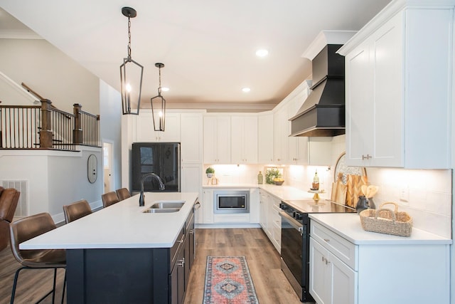 kitchen with black electric range oven, custom exhaust hood, sink, white cabinetry, and a center island with sink