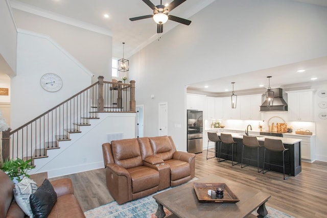 living room featuring sink, light hardwood / wood-style floors, a towering ceiling, and ornamental molding