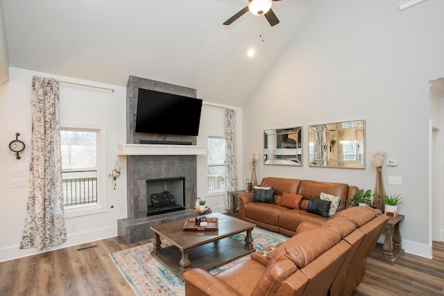 living room with ceiling fan, high vaulted ceiling, a tile fireplace, and wood-type flooring