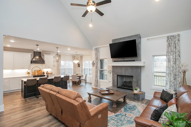 living room featuring a tiled fireplace, light hardwood / wood-style floors, high vaulted ceiling, and ceiling fan