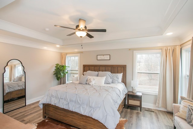 bedroom with ceiling fan, wood-type flooring, and a tray ceiling