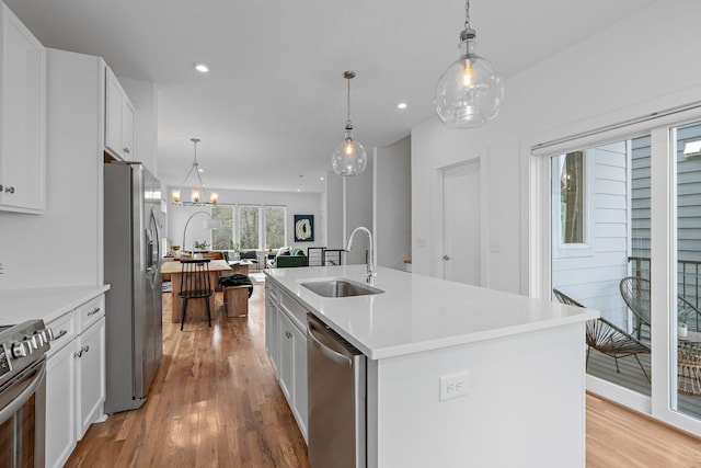 kitchen featuring appliances with stainless steel finishes, sink, decorative light fixtures, white cabinets, and a center island with sink