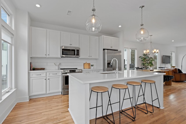 kitchen with white cabinets, a center island with sink, appliances with stainless steel finishes, and pendant lighting