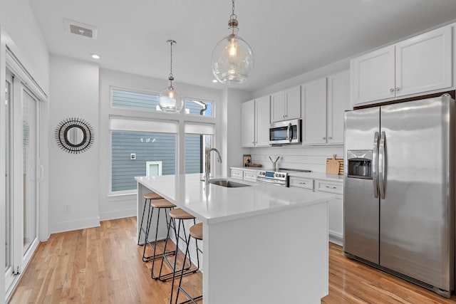 kitchen with white cabinetry, sink, pendant lighting, stainless steel appliances, and a center island with sink