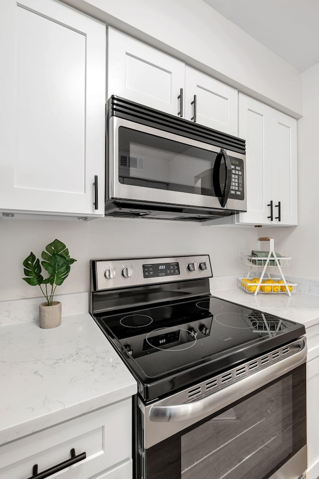 kitchen with light stone countertops, white cabinetry, and stainless steel appliances