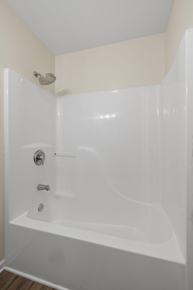 bathroom with wood-type flooring, washtub / shower combination, and a textured ceiling