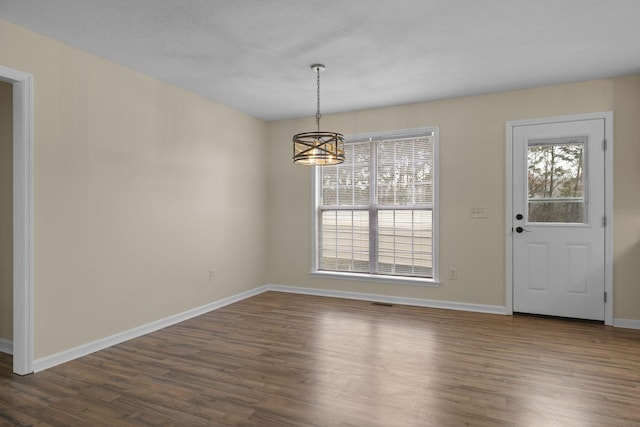 unfurnished dining area featuring a chandelier and dark hardwood / wood-style floors