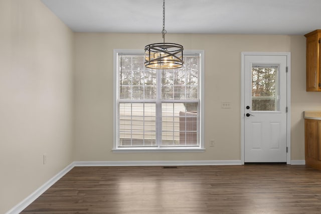 unfurnished dining area featuring a notable chandelier, a healthy amount of sunlight, and dark hardwood / wood-style floors