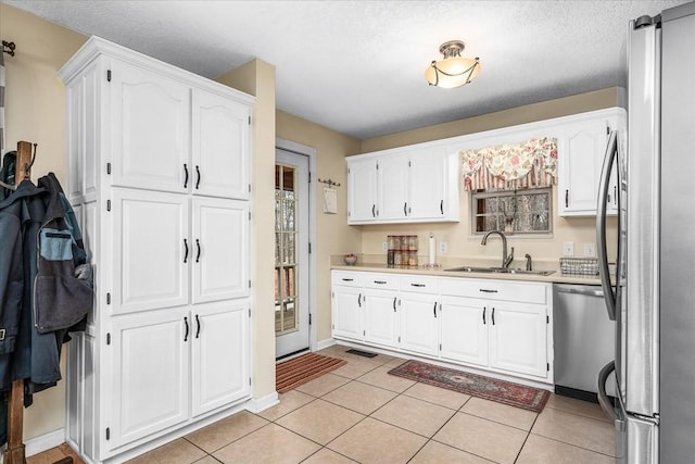 kitchen with appliances with stainless steel finishes, a textured ceiling, white cabinetry, light tile patterned floors, and sink