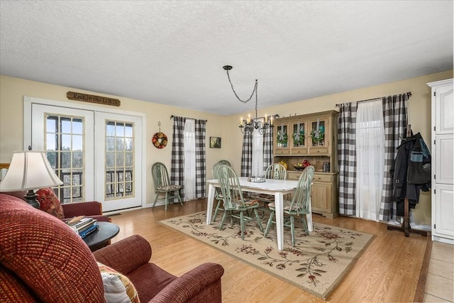 dining room with a notable chandelier, light wood-type flooring, and a textured ceiling