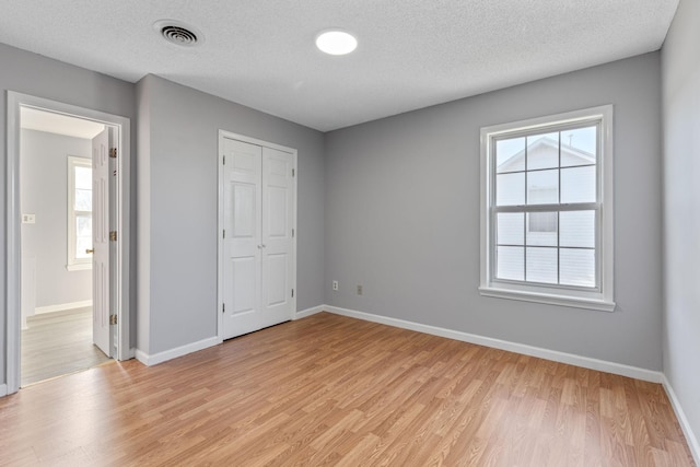 unfurnished bedroom featuring multiple windows, a textured ceiling, and light hardwood / wood-style floors