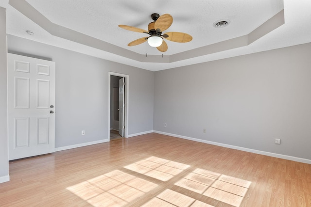 unfurnished room featuring ceiling fan, light hardwood / wood-style floors, a textured ceiling, and a tray ceiling