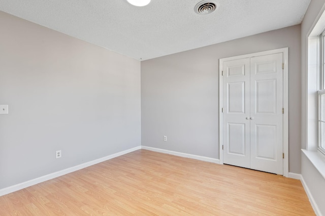 unfurnished bedroom with a textured ceiling, a closet, and light hardwood / wood-style flooring