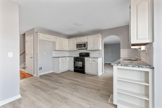 kitchen featuring sink, backsplash, white cabinets, and black gas range