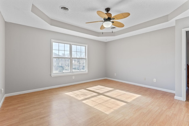 unfurnished room featuring ceiling fan, a textured ceiling, a tray ceiling, and light hardwood / wood-style flooring