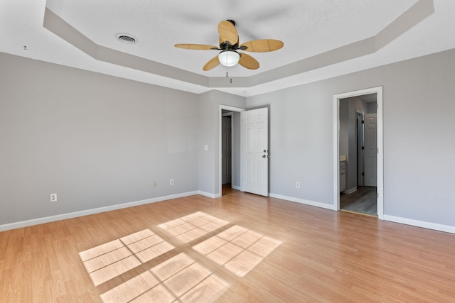 unfurnished bedroom with ceiling fan, light hardwood / wood-style flooring, and a raised ceiling