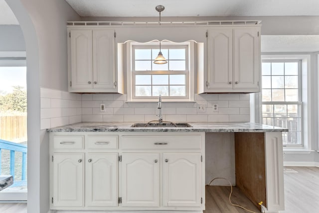 kitchen featuring tasteful backsplash, sink, decorative light fixtures, white cabinets, and light wood-type flooring