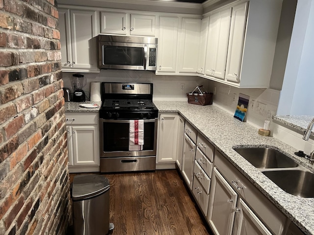 kitchen featuring sink, stainless steel appliances, light stone countertops, and brick wall