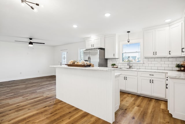 kitchen featuring a center island, white cabinetry, sink, decorative light fixtures, and stainless steel fridge