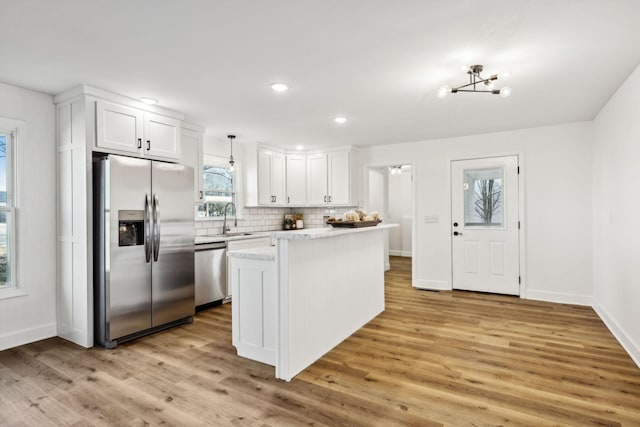 kitchen with a kitchen island, white cabinetry, stainless steel appliances, sink, and hanging light fixtures