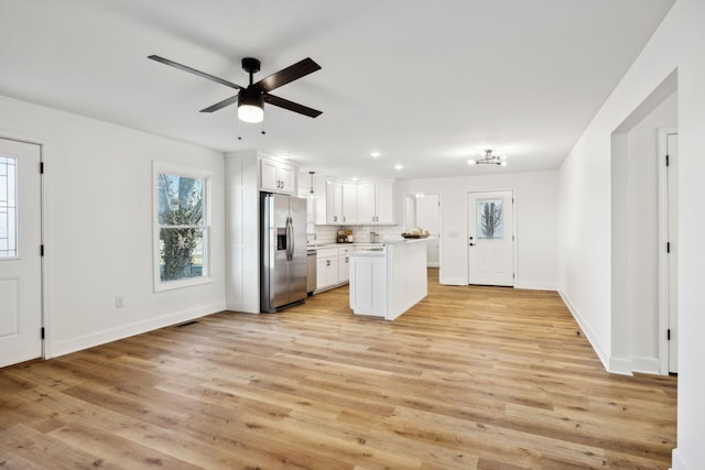 kitchen featuring decorative backsplash, stainless steel refrigerator with ice dispenser, white cabinets, a kitchen island, and light wood-type flooring